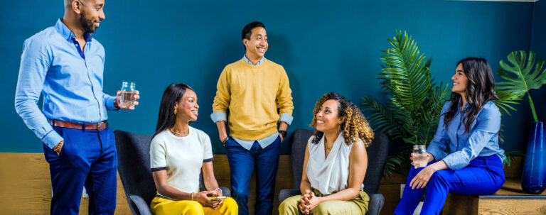 Business people sit and stand by a blue wall as they discuss target personas.