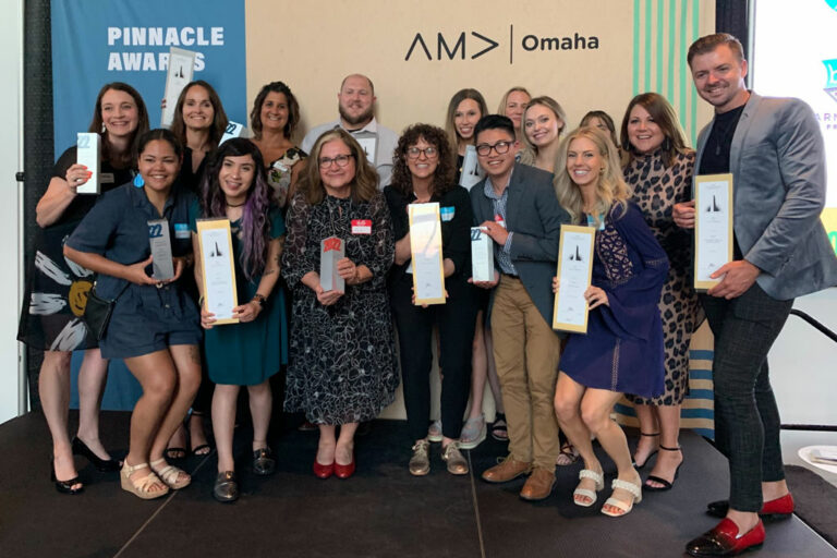 A group of KidGlov employees hold up awards on the stage at AMA Omaha's Pinnacle Awards.