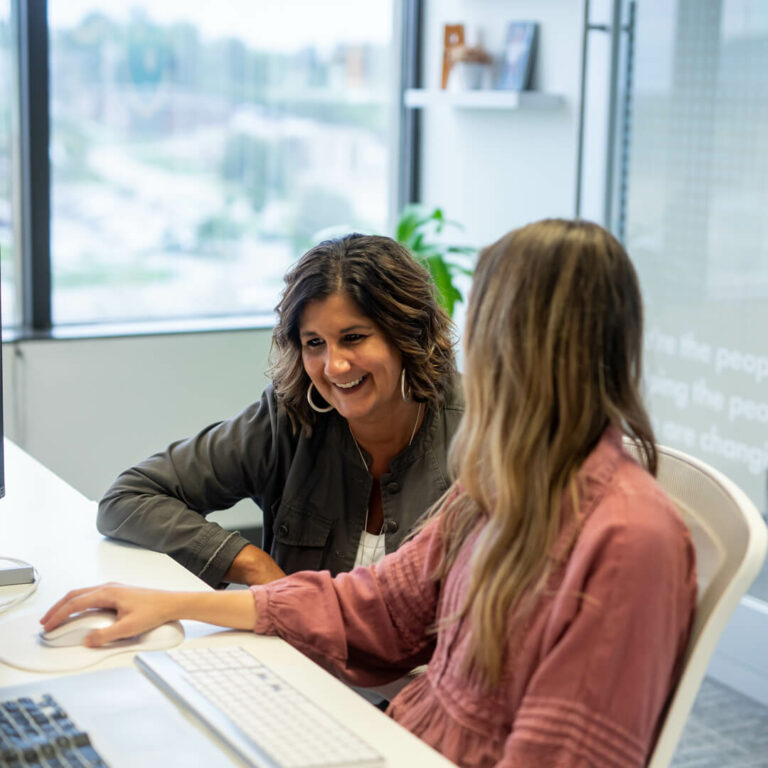 Two women work on a computer together in the KidGlov office.