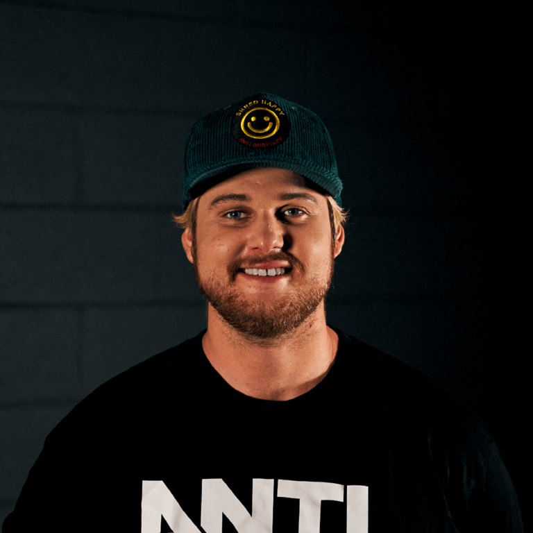 Headshot of Rob Joseph smiling in front of a black background. He is wearing a black baseball cap and black t-shirt.