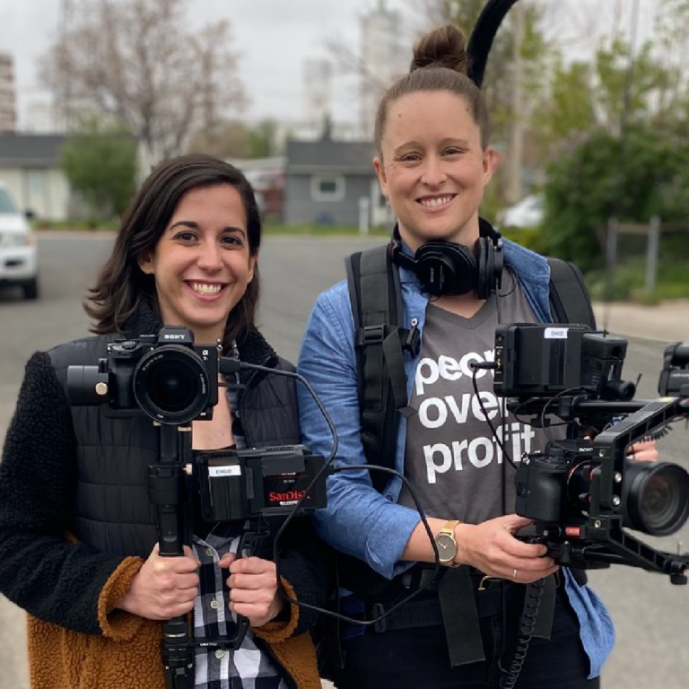 Two women hold video cameras while smiling.