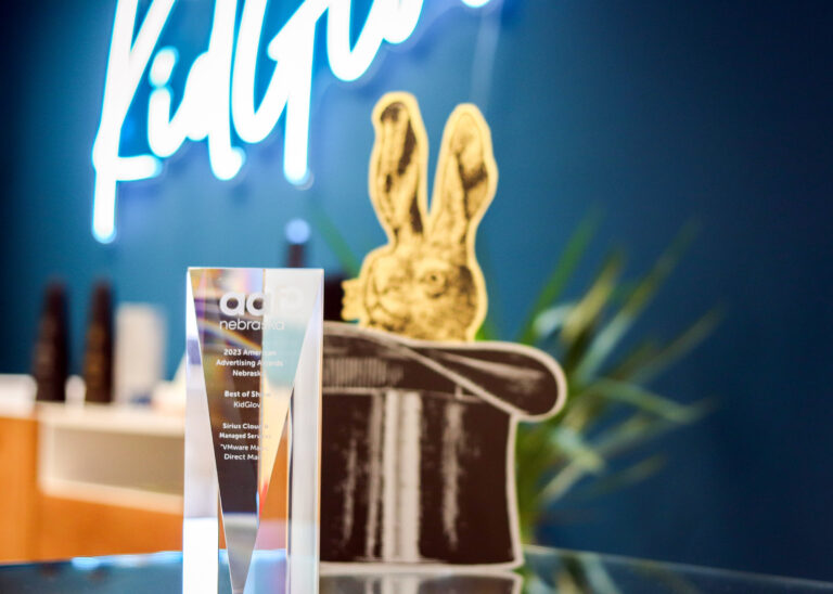 A crystal trophy sits next to a printed brochure cut in the shape of a rabbit coming out of a magician's hat. The trophy reads 2023 American Advertising Awards, Best of Show, KidGlov, Sirius Cloud & Managed Service, "VMware Magic Direct Mail"