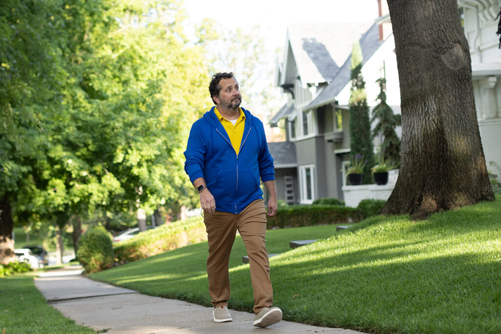 Man wearing a blue hoodie and yellow polo walks down a beautiful neighborhood street