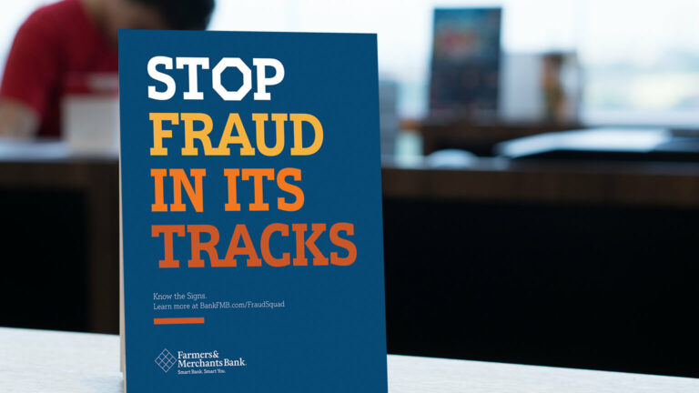 Blue Farmer's and Merchant's Bank sign that says "Stop Fraud In Its Tracks" in orange lettering