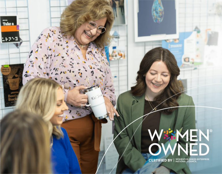 Lyn, the owner of KidGlov, talks joyfully with a group of female employees. The Certified Women-Owned Business seal is in the corner.